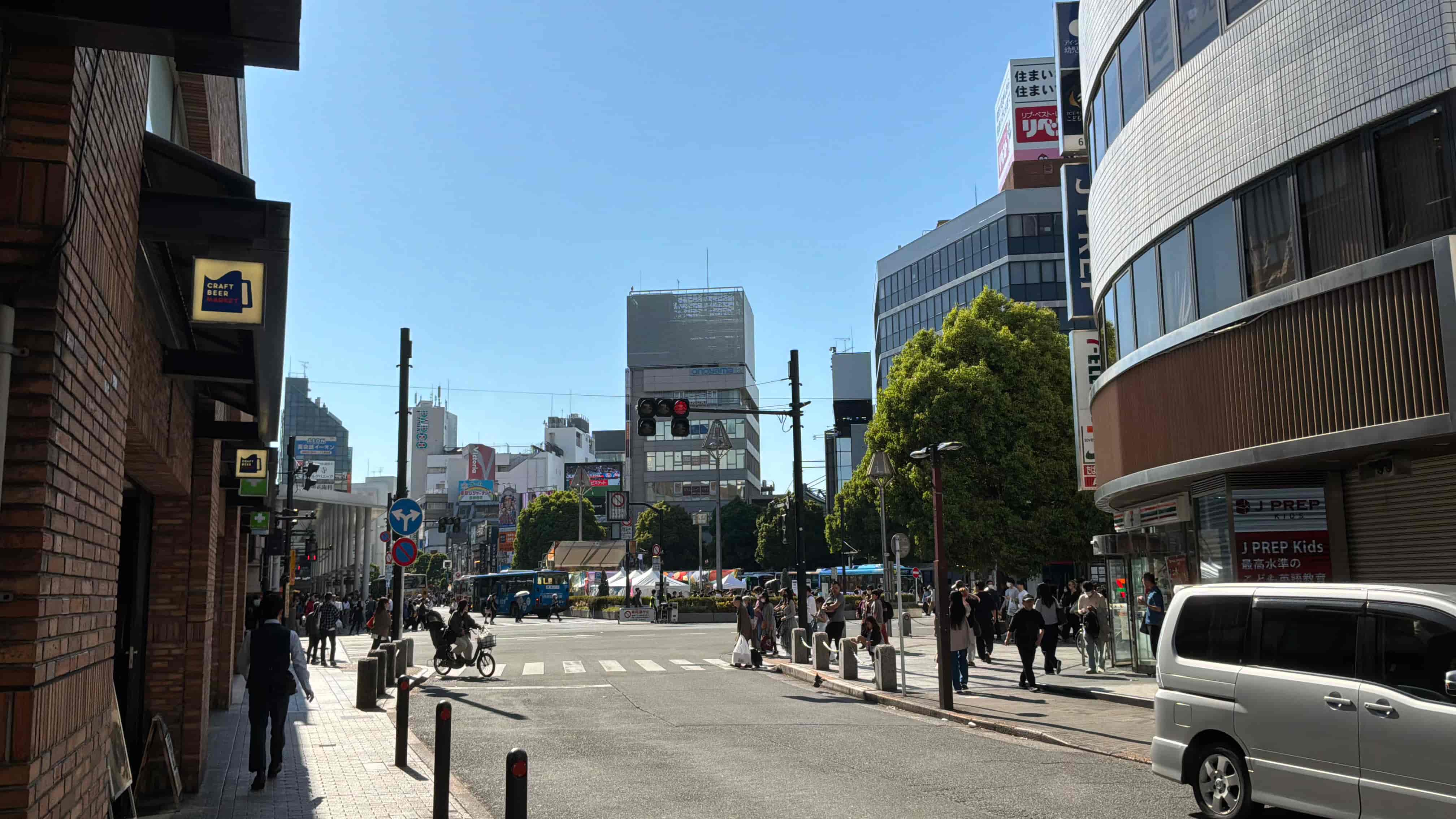 晴天下的吉祥寺街道路口，兩旁是商業大樓，行人正穿越馬路